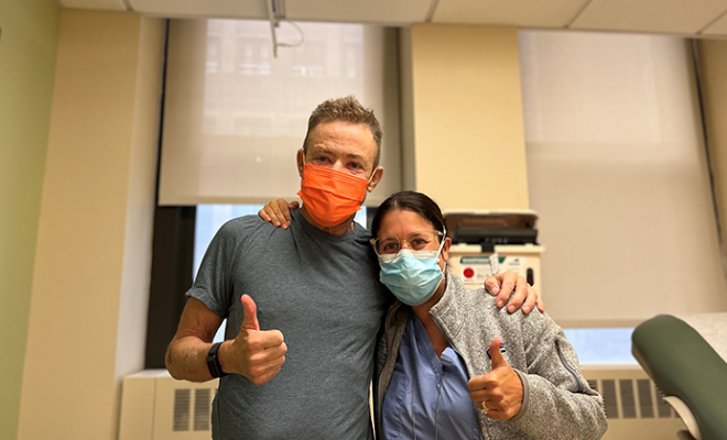 Jerry smiling with a thumbs up with his nurse in the hospital while wearing a mask.