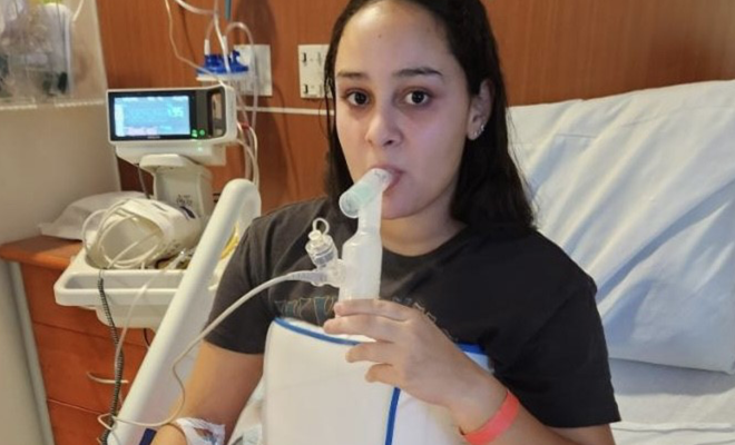 Natalie using a nebulizer and vest in a hospital bed 