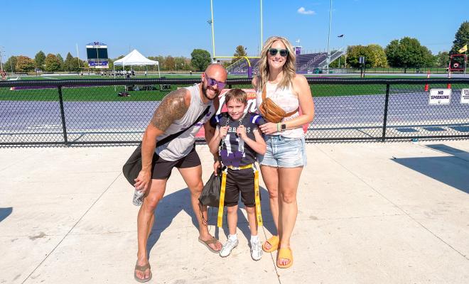 Jaclyn smiling with her husband and her son, Major, in front of a football field
