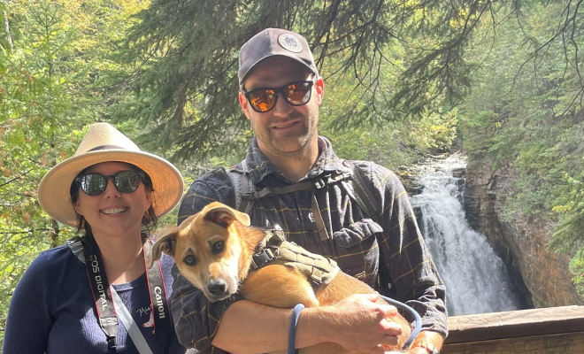 Meagan and her husband and dog on a hike standing near a waterfall